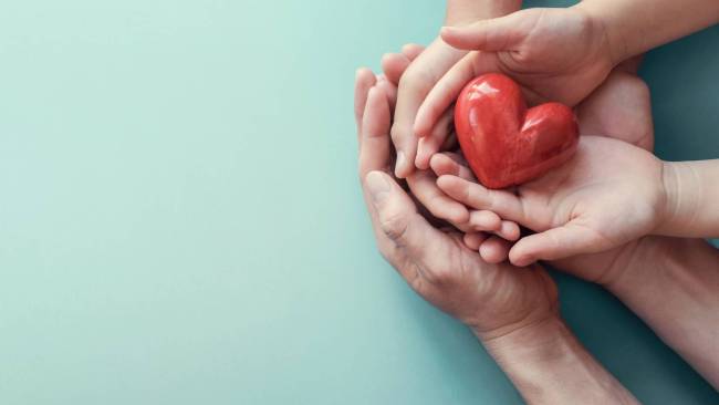 Les mains de plusieurs personnes tenant ensemble la représentation d'un coeur rouge